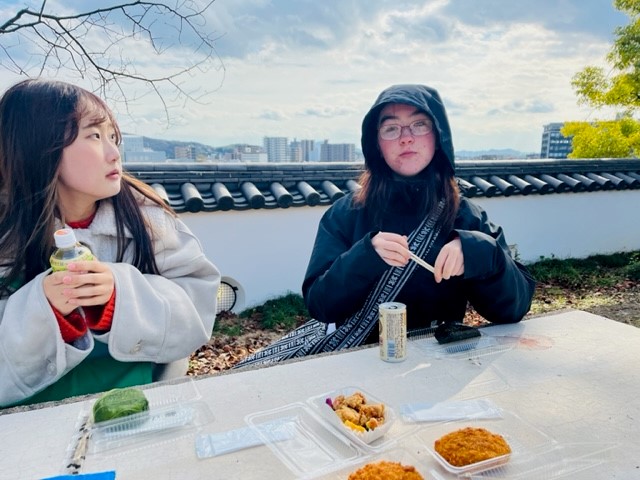 互いの国の食文化について語らいながら昼食を食べる二人の様子 左から堤さんとRowanさん（岡山城にて）