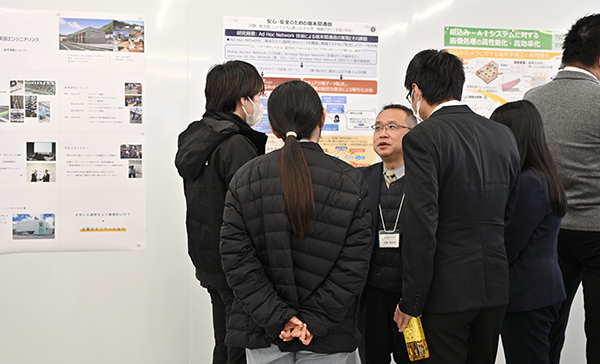 「安心・安全のための端末間通信」と題して発表し、ポスターの前で質問に答える河野英太郎教授