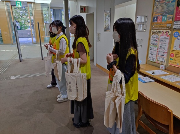 1F閲覧室入口での配布の様子です。イベントのスタッフとわかるよう、県立図書館のゼッケンをお借りしました。